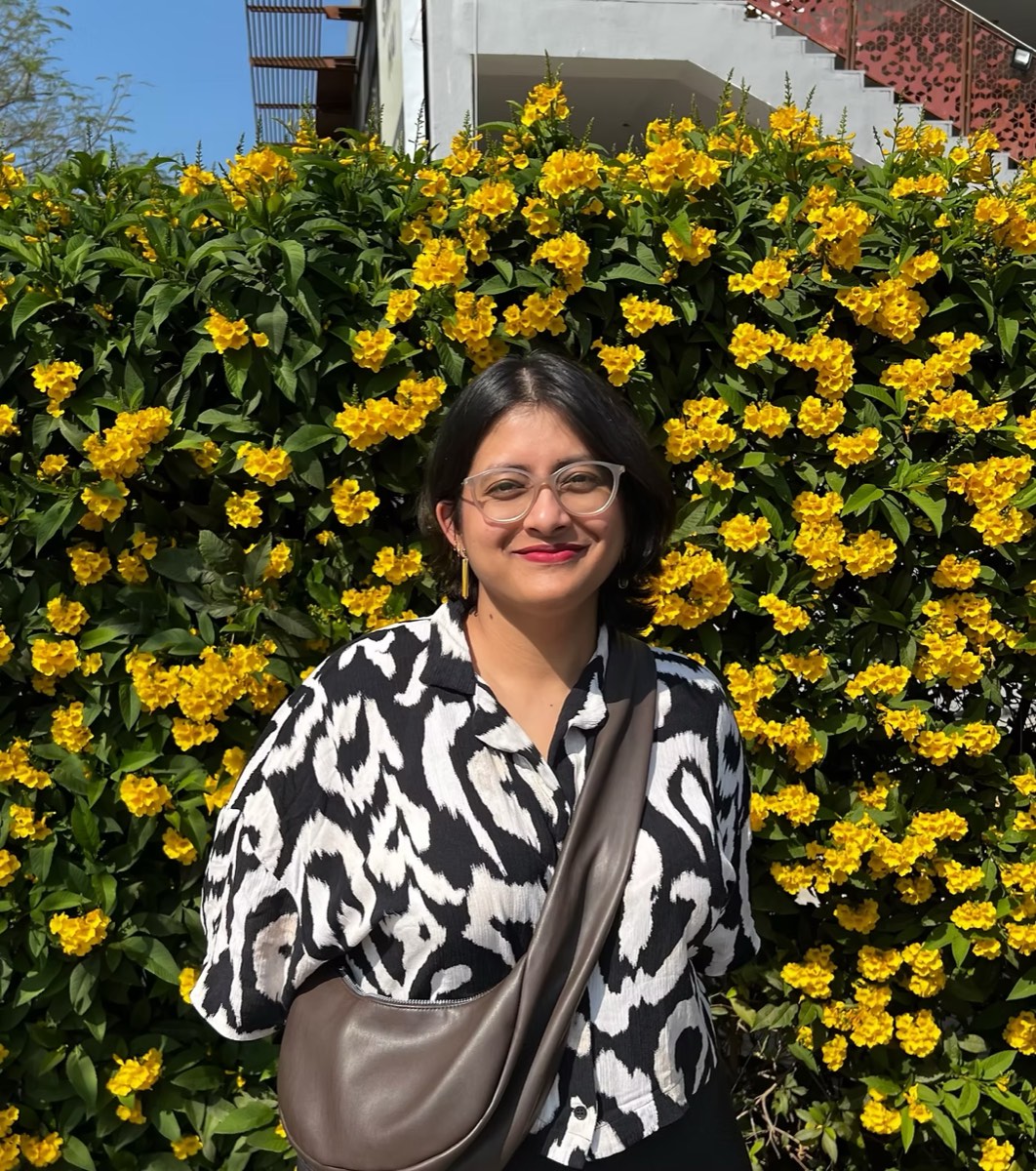 Anisha Mazumder, smiling in front of a wall of yellow flowers